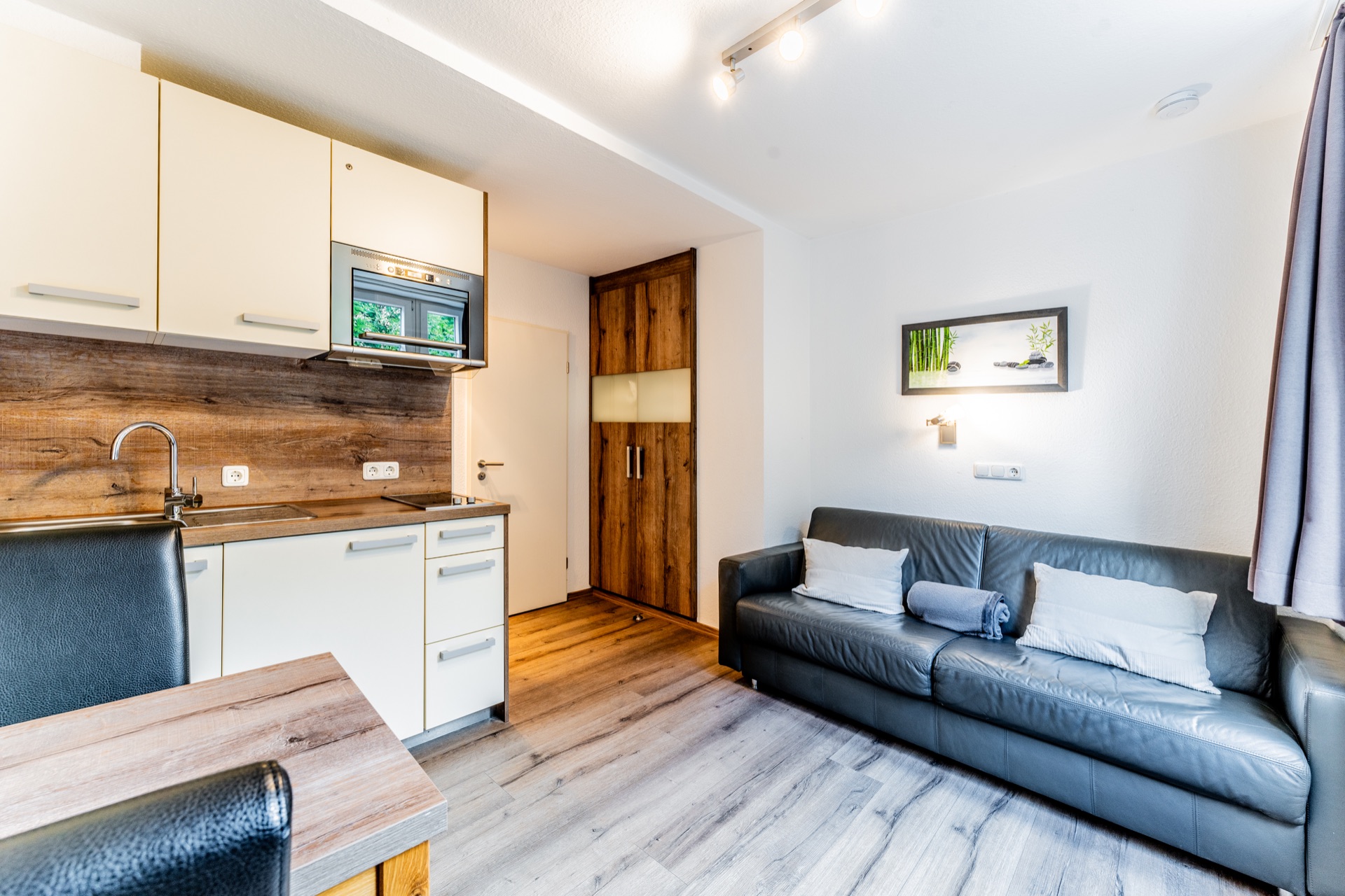 Heller Raum mit Küchenzeile, Holzboden, grauem Sofa und Wandbild.