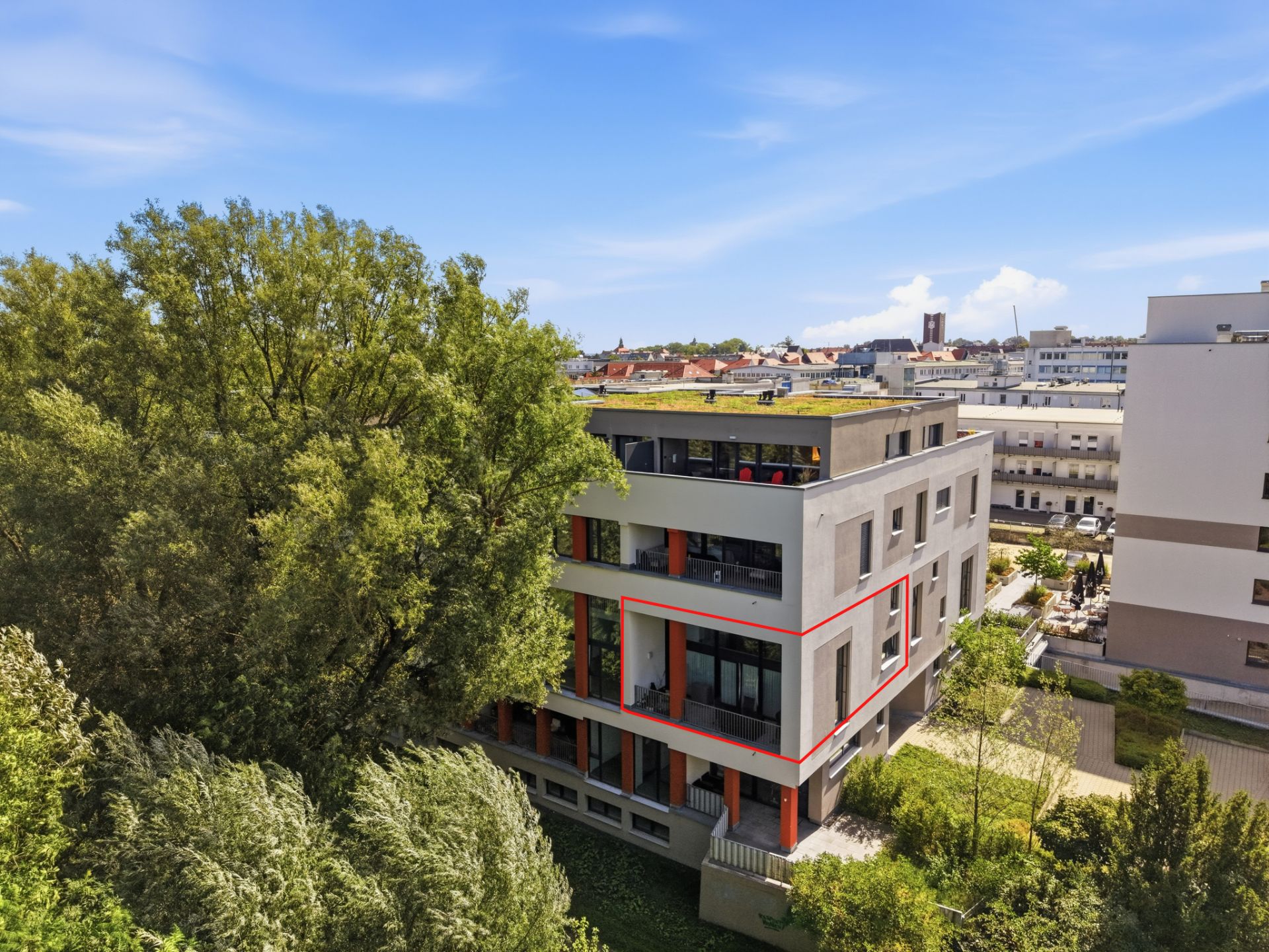 Modernes Mehrfamilienhaus mit Flachdach und umliegenden Bäumen bei klarem Himmel.