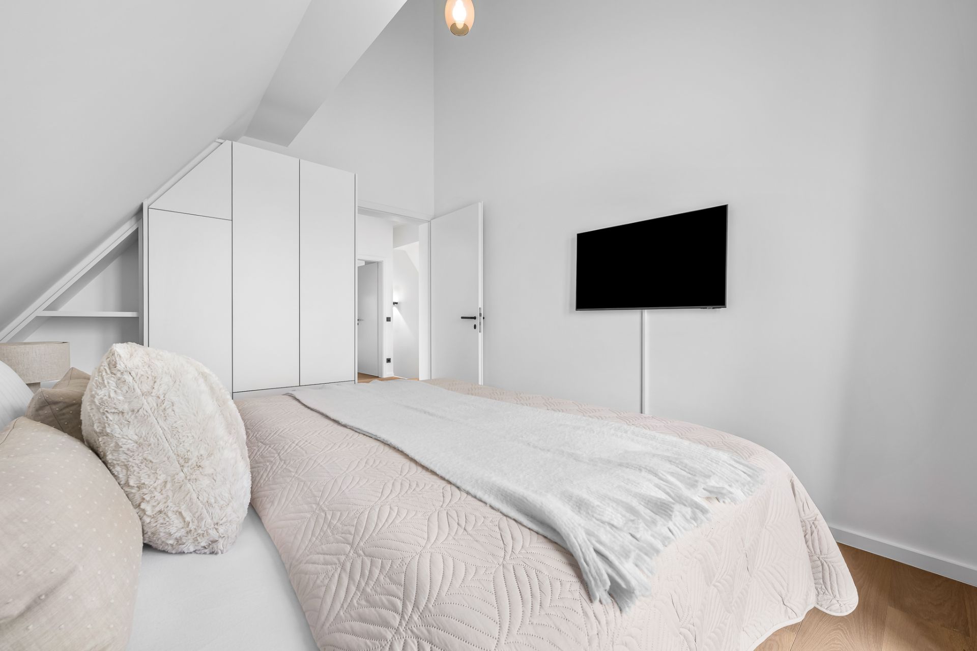 Helles Schlafzimmer mit Doppelbett, Wandfernseher und weißem Einbauschrank.
