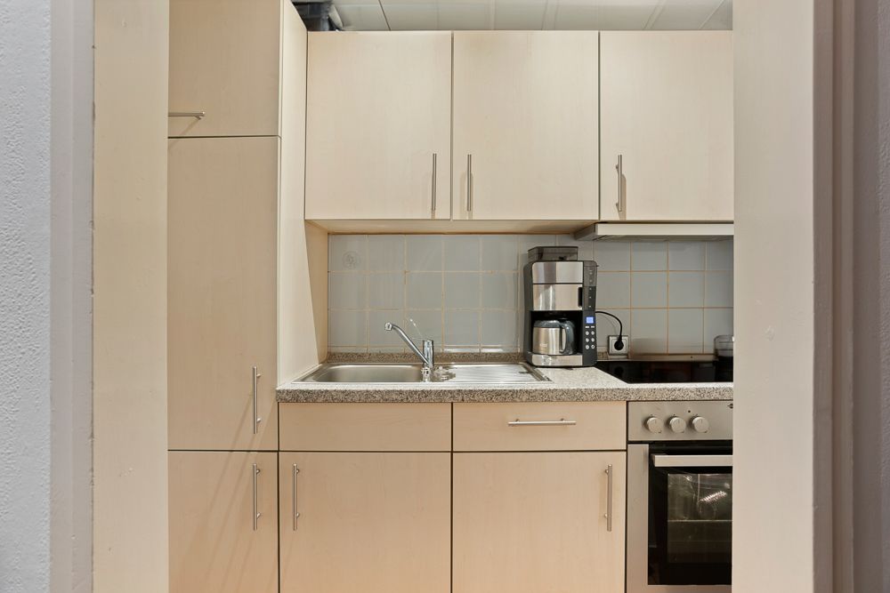 Moderne Einbauküche mit Spüle, Herd, Backofen und Kaffeemaschine, helle Holzfronten.