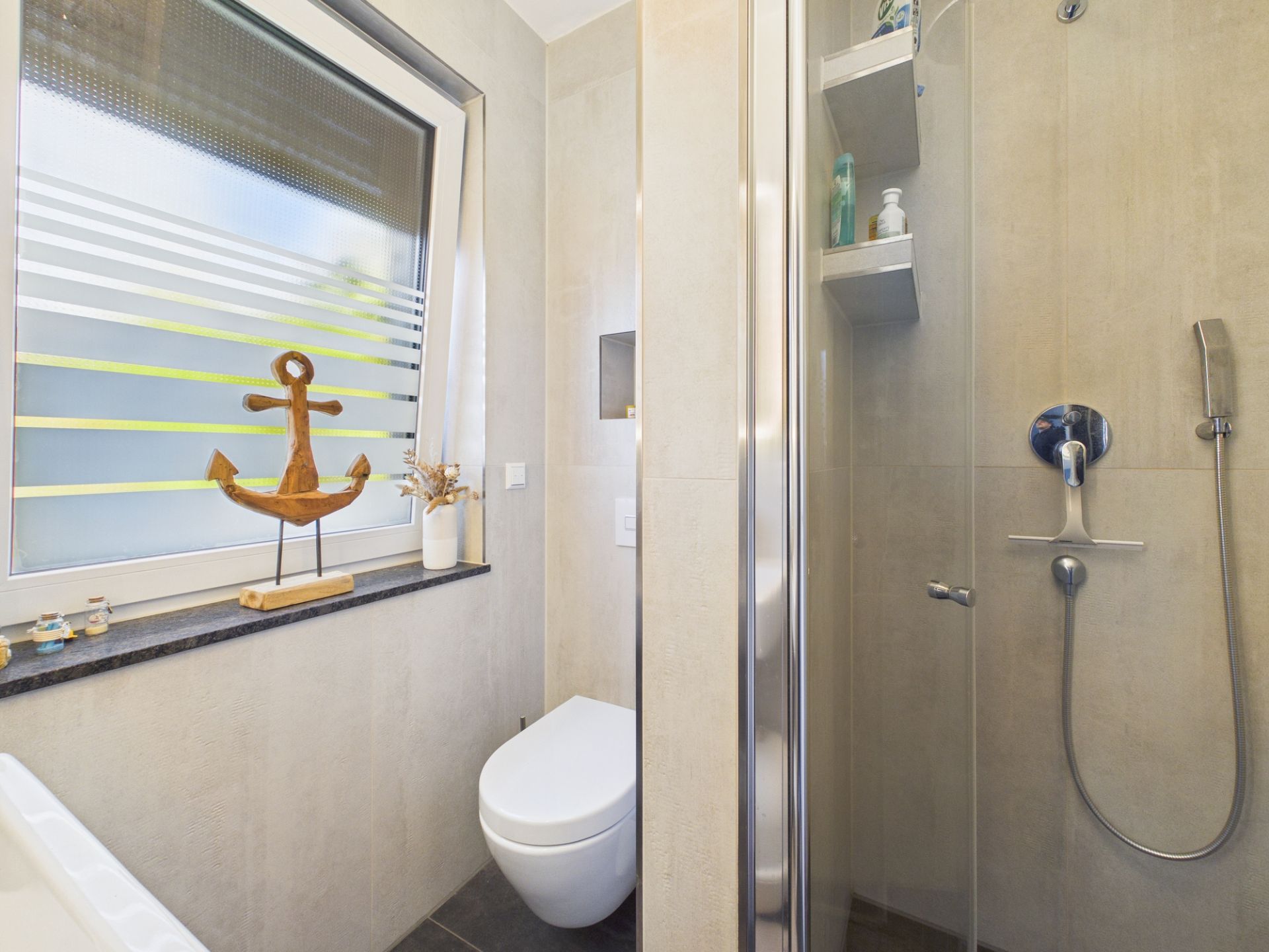 Modernes Badezimmer mit Dusche, Toilette und Fenster mit Dekoration.