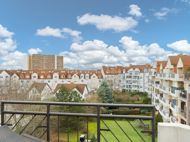 Blick von einem Balkon auf Wohngebäude mit roten Dächern und einen grünen Innenhof.