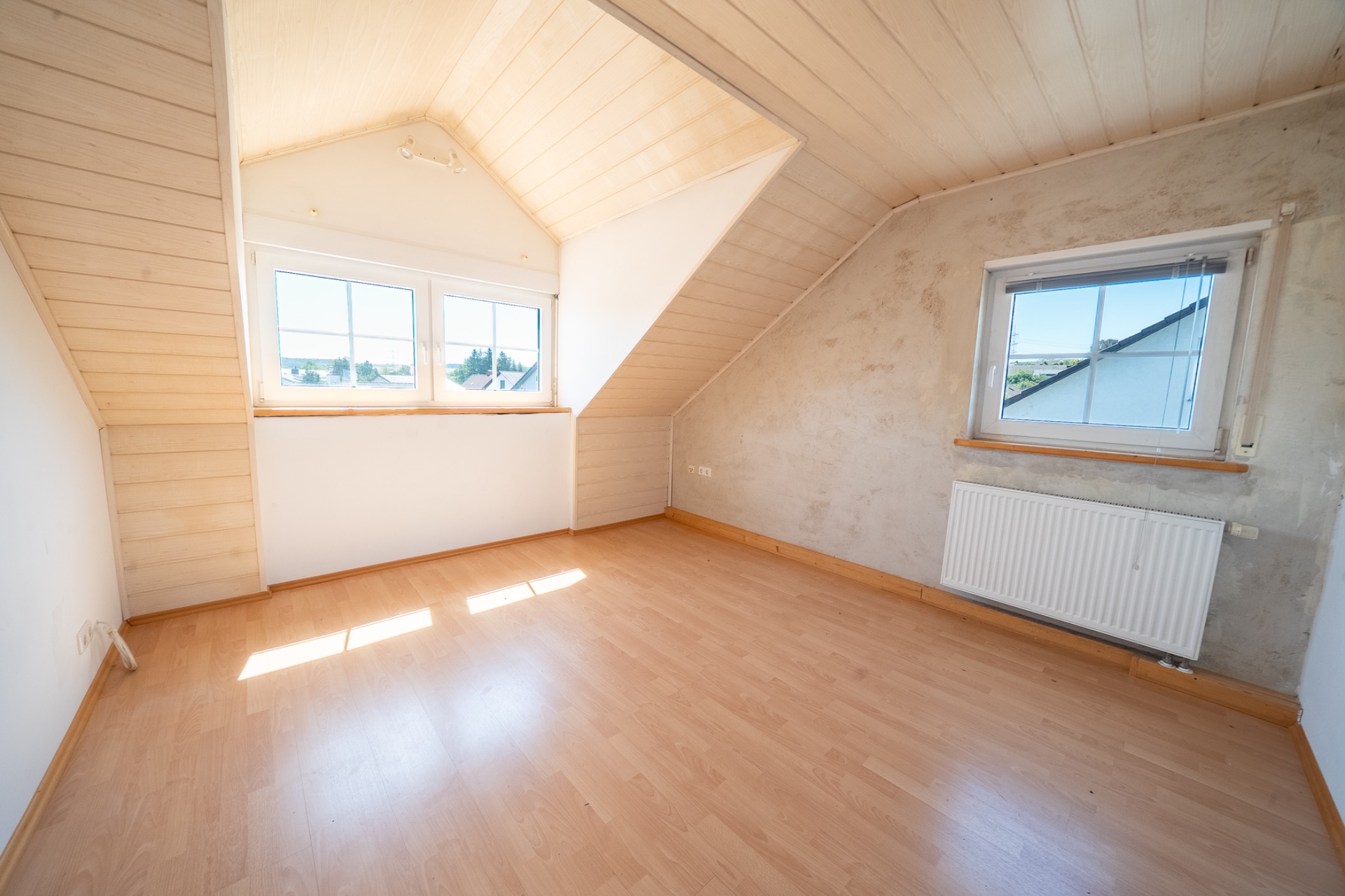 Helles Zimmer mit Dachschräge, großen Fenstern und Laminatboden.