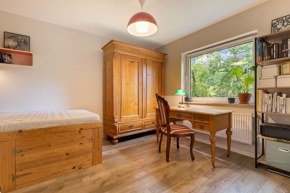 Helles Zimmer mit Holzbett, Kleiderschrank, Schreibtisch, Stuhl, Regal und großem Fenster.