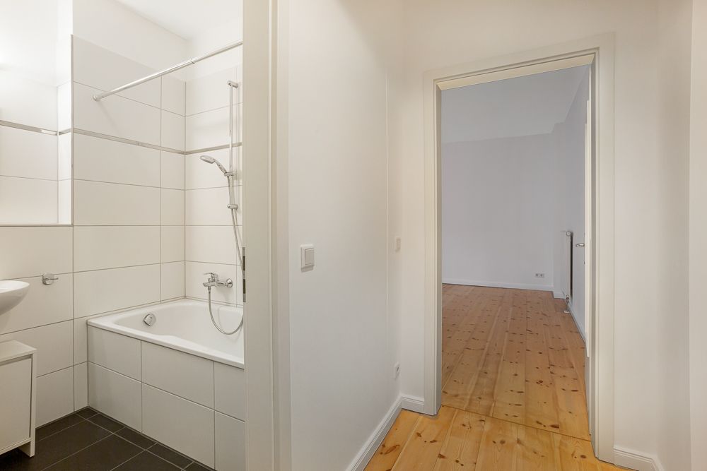 Helles Badezimmer mit Badewanne und Dusche, daneben Flur mit Holzboden.