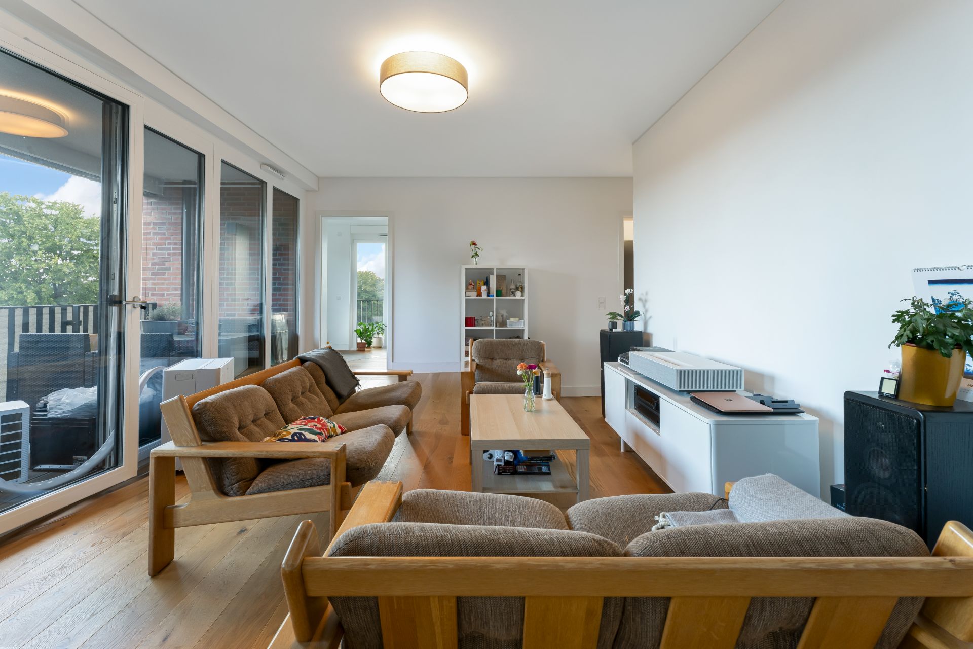 Helles Wohnzimmer mit Holzboden, Sofa, Sesseln, Couchtisch und großen Fenstern zum Balkon.