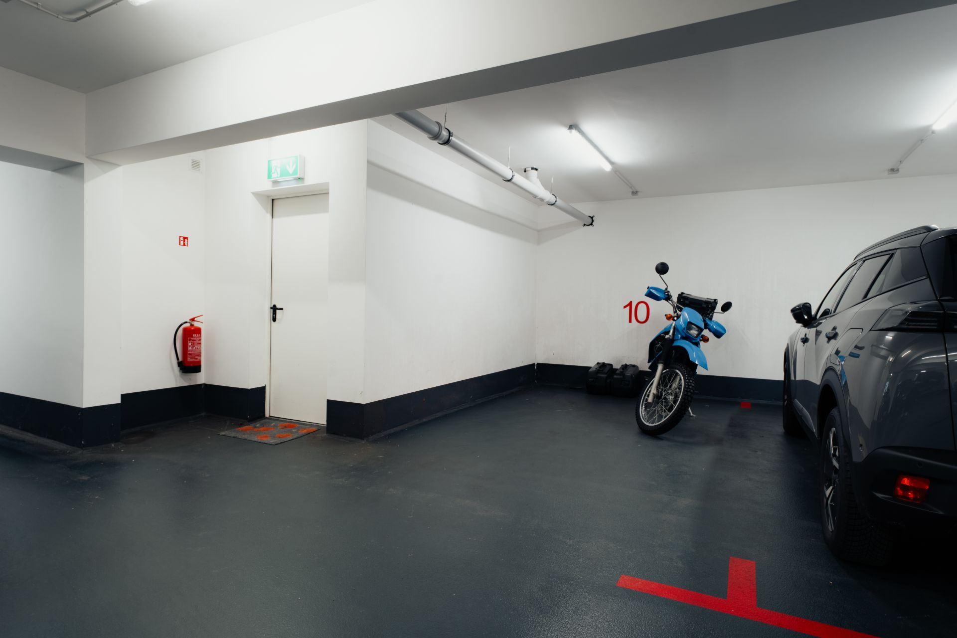 Tiefgaragenstellplatz mit Motorrad, Auto, Feuerlöscher und weißer Tür.