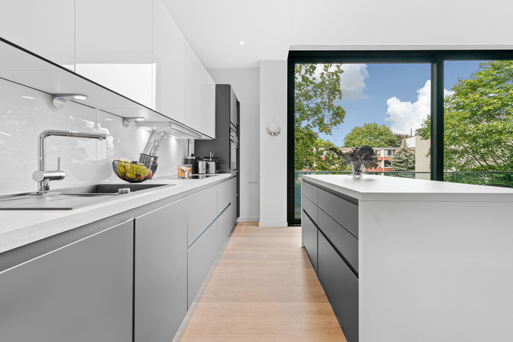 Moderne Küche mit grauen Schränken, Kochinsel und großem Fenster mit Blick ins Grüne.