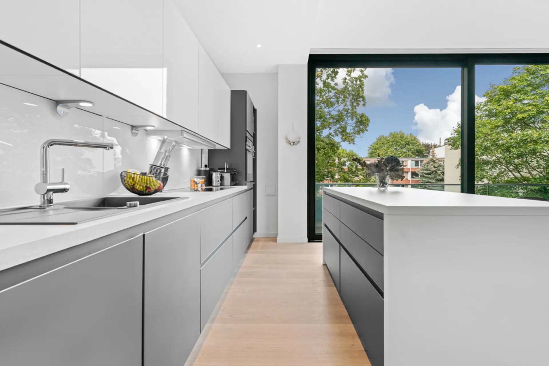 Moderne Küche mit grauen Schränken, Kochinsel und großem Fenster mit Blick ins Grüne.