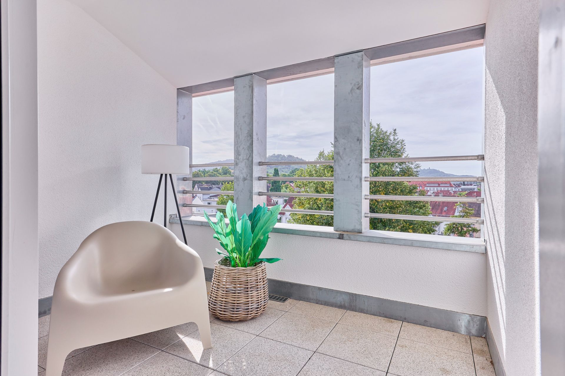 Helle Loggia mit Stuhl, Stehlampe und Pflanze im Korb, Ausblick ins Grüne.
