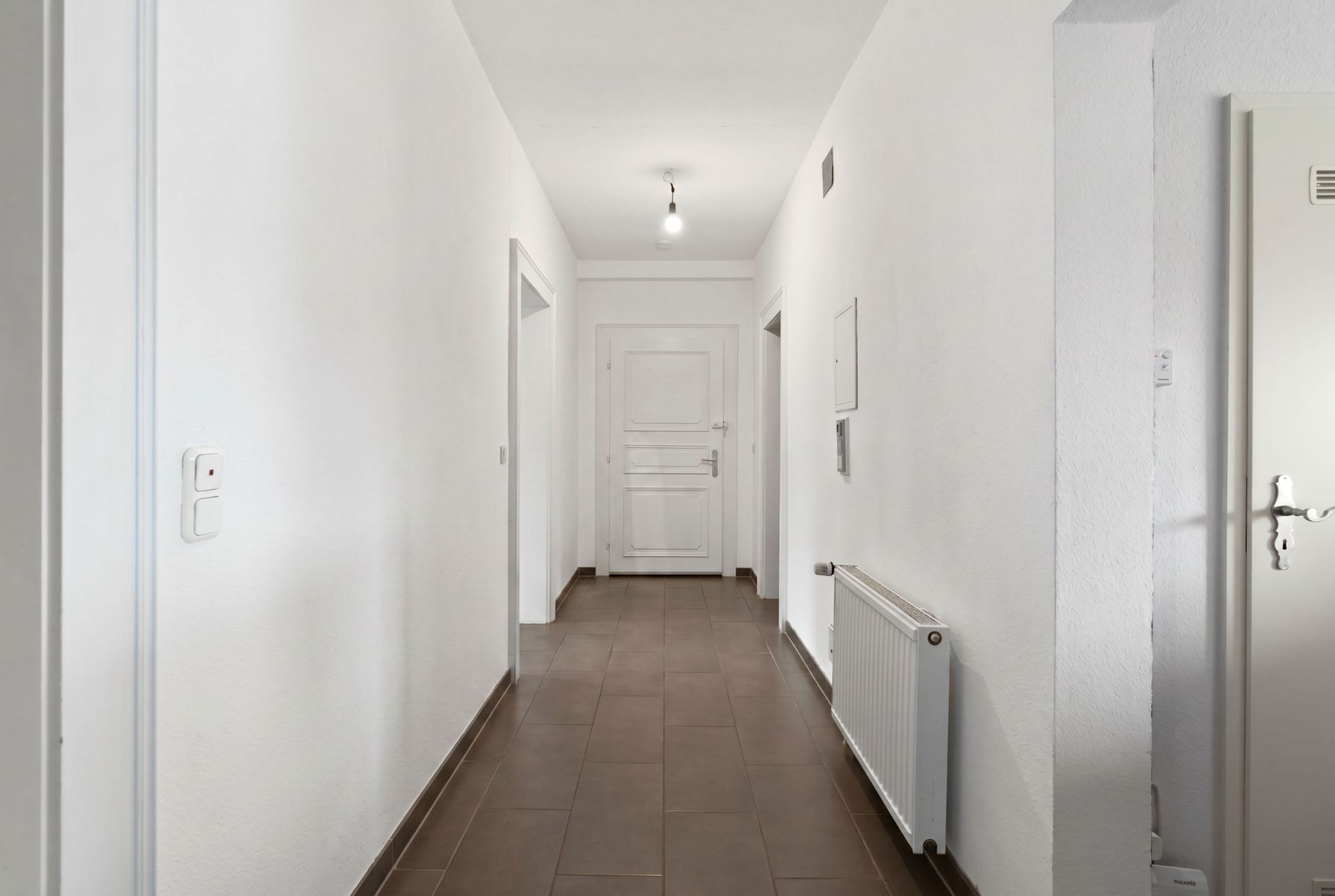 Heller Flur mit braunem Boden, weißen Wänden und einer weißen Tür am Ende.