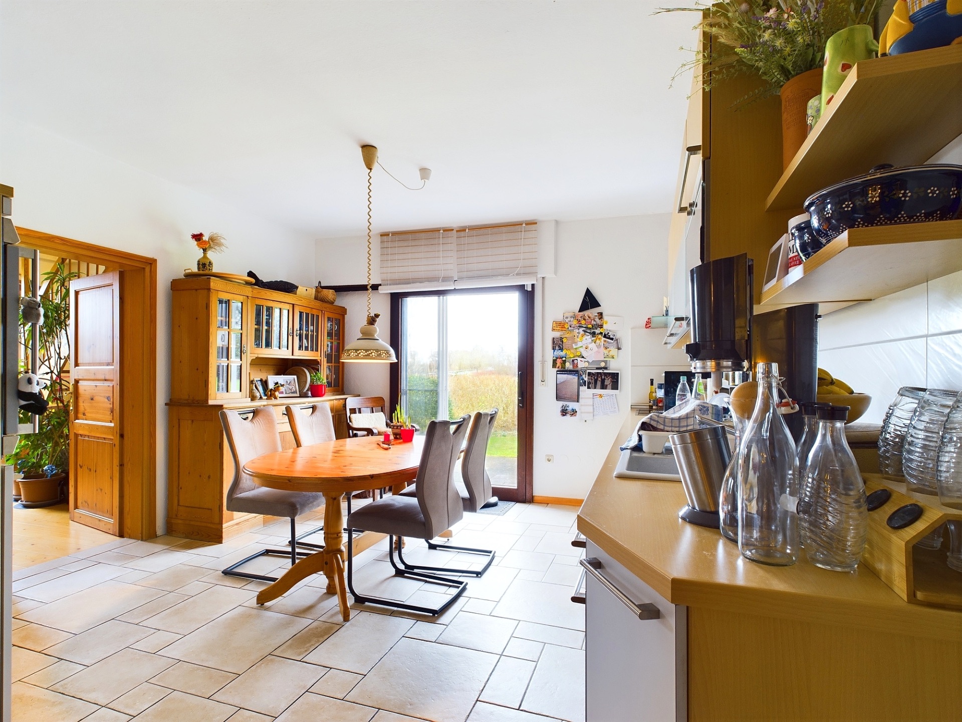 Helle Wohnküche mit Esstisch, Stühlen, Holzschränken und großen Fenstern zum Garten.