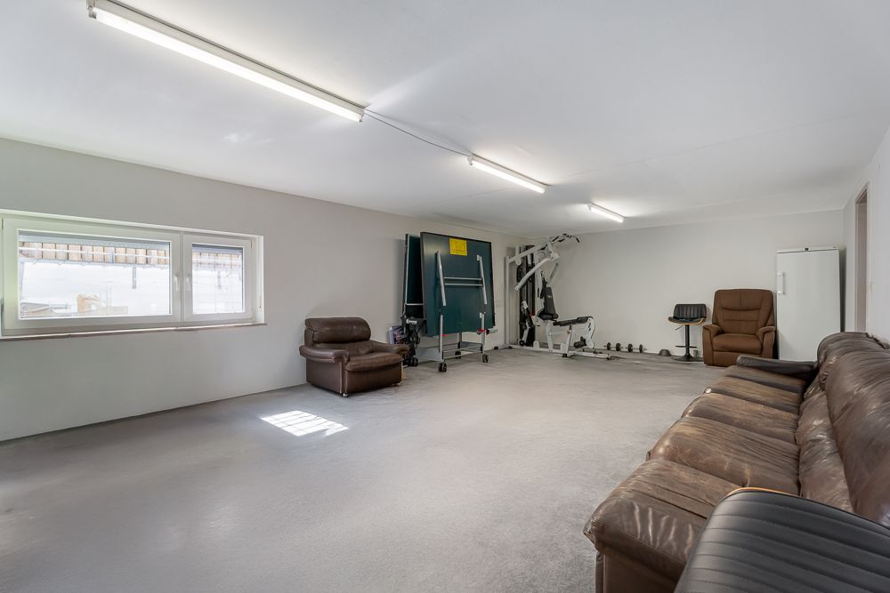 Großer Raum mit braunem Ledersofa, Fitnessgeräten und einem Fenster an der Wand.