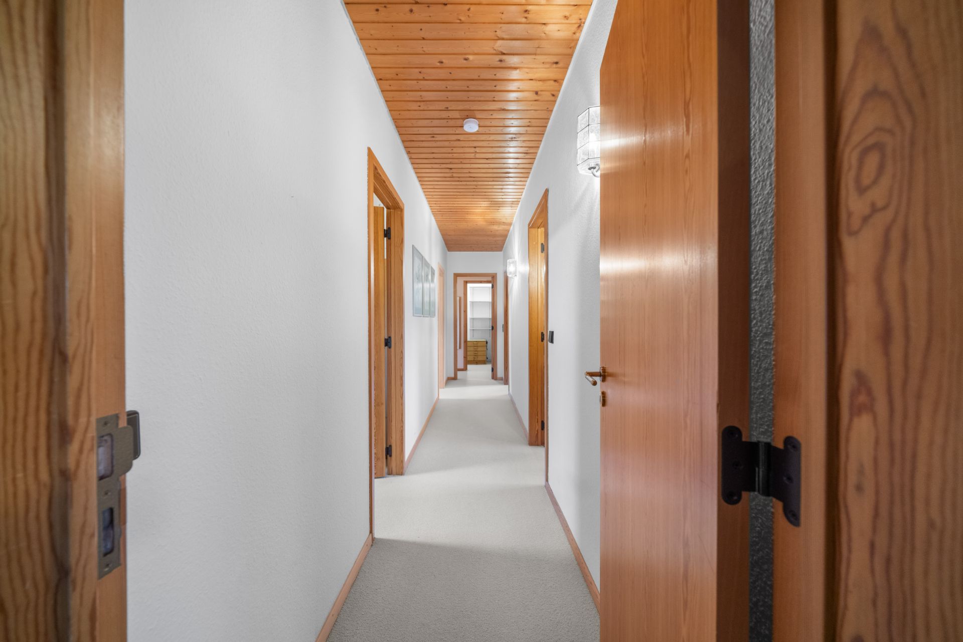 Langer, heller Flur mit Holztüren und Holzdecke in einem Wohnhaus.