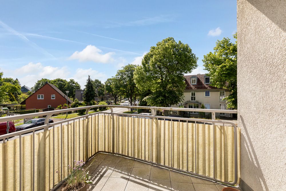 Balkon mit Geländer und Blick auf eine ruhige Straße mit Bäumen und Wohnhäusern.