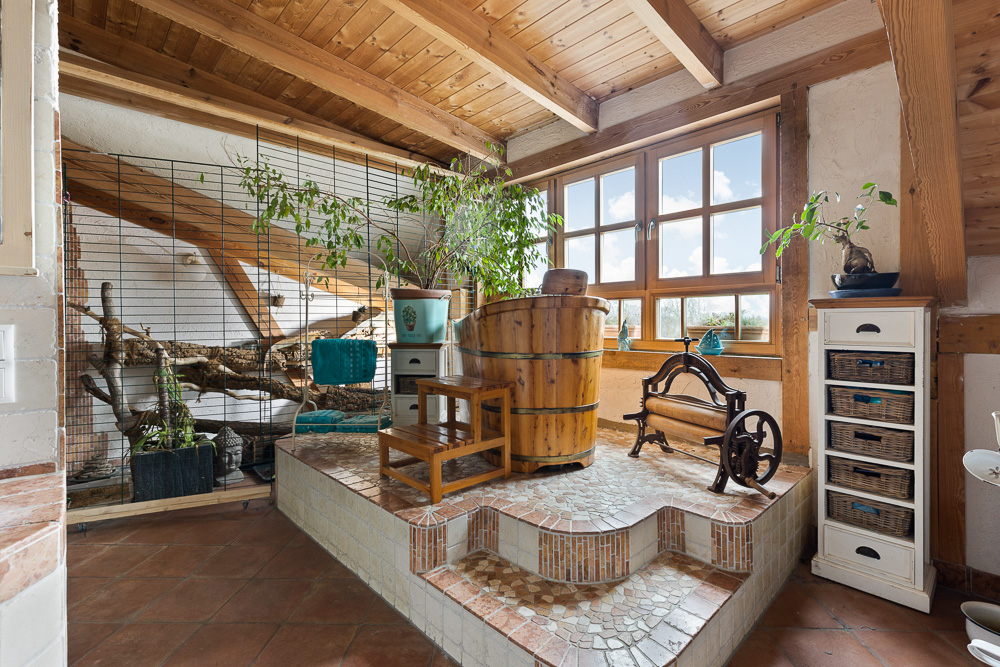 Raum mit Holzbottich-Badewanne, Pflanzen, großem Fenster und gefliestem Podest.