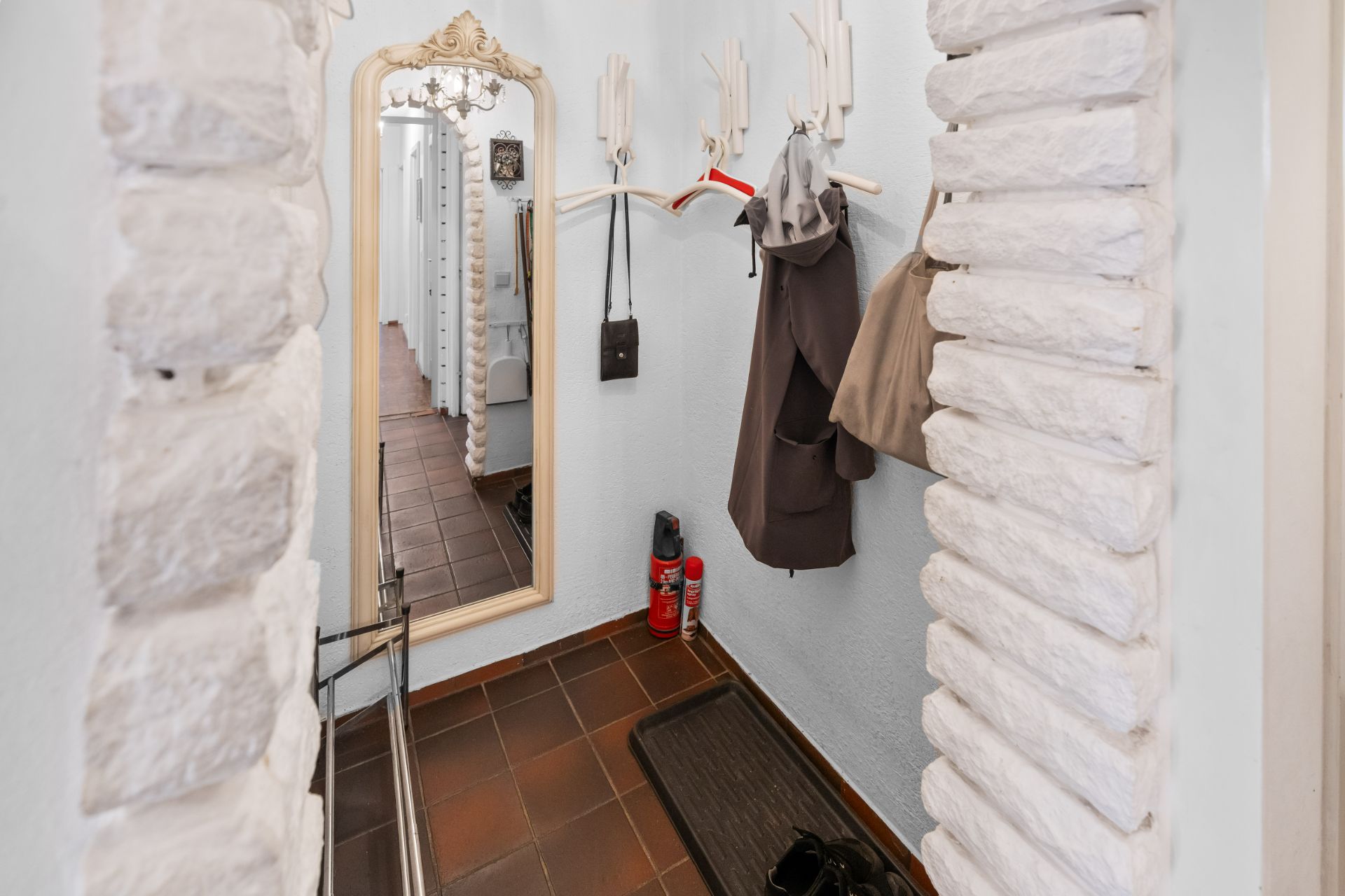 Schmaler Flur mit Spiegel, Garderobe, Jacken, Haken und zwei Feuerlöschern an der Wand.