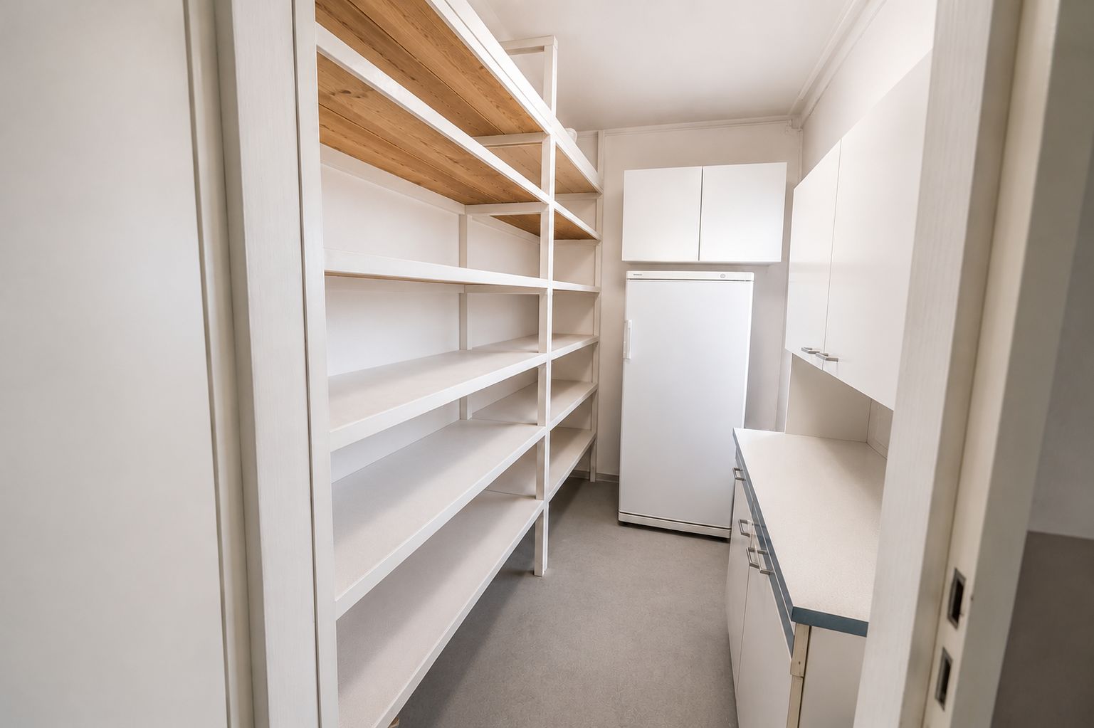 Hauswirtschaftsraum mit offenen Regalen, Kühlschrank und weißen Schränken.