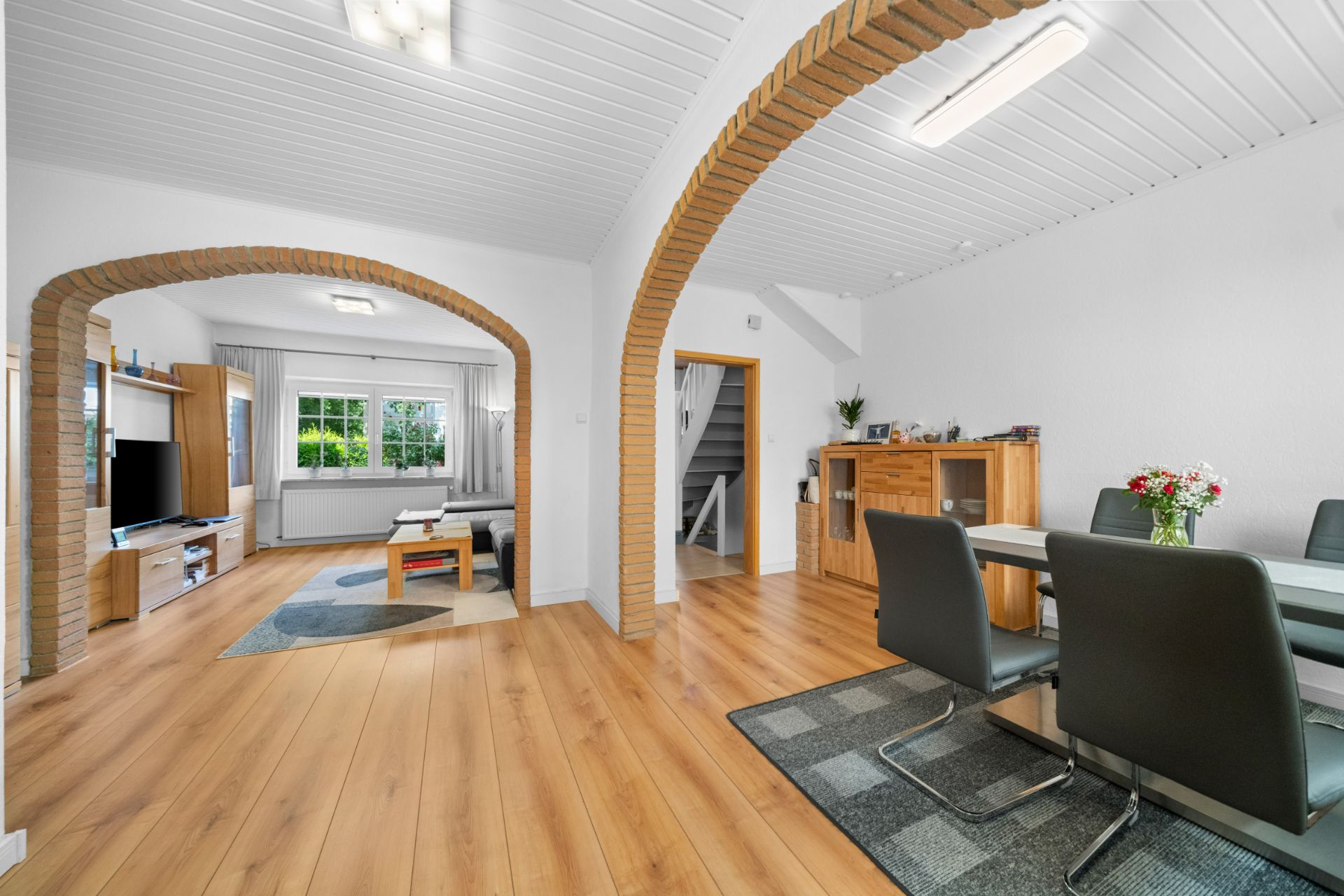 Helles Wohnzimmer mit Essbereich, Holzboden, zwei Rundbögen und großem Fenster.