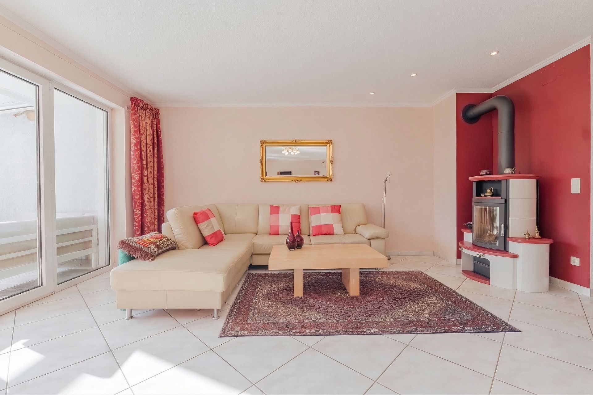Helles Wohnzimmer mit Ecksofa, Couchtisch, Teppich, Kaminofen und großer Fensterfront.