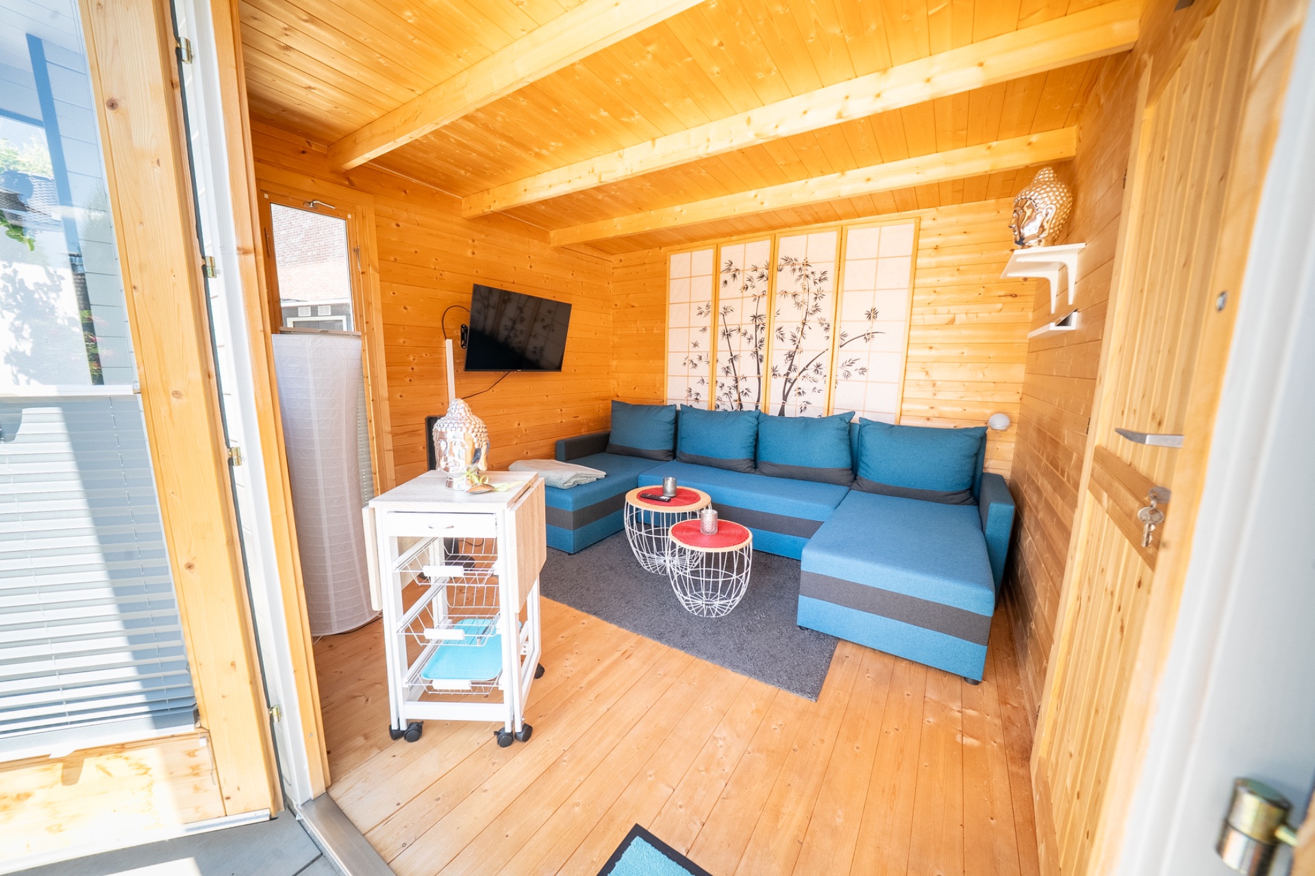 Helles Holzwohnzimmer mit blauer Eckcouch, Wanddekoration, kleinem Tisch und TV.