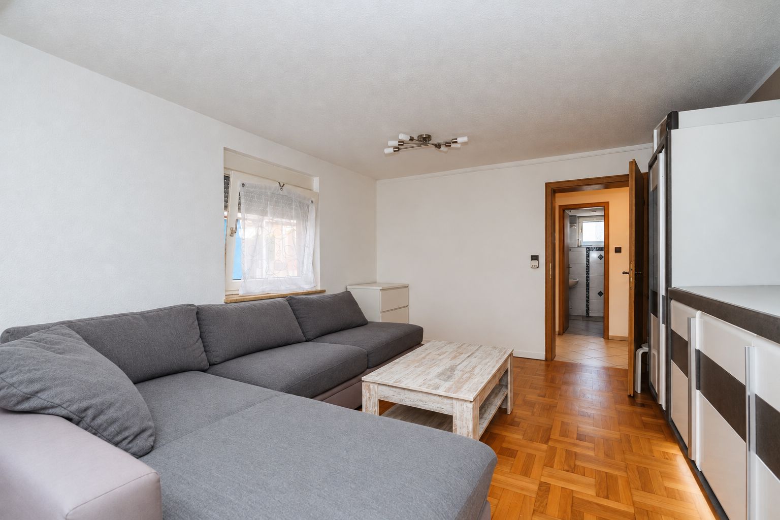 Wohnzimmer mit grauem Ecksofa, weißem Couchtisch und Parkettboden.
