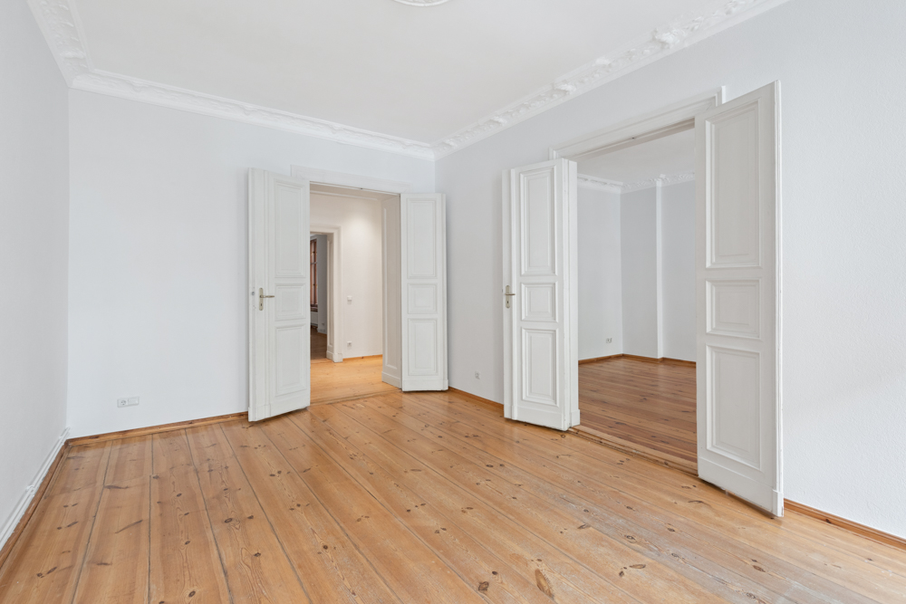 Leerer Raum mit Holzboden, weißen Wänden und offenen Doppeltüren.