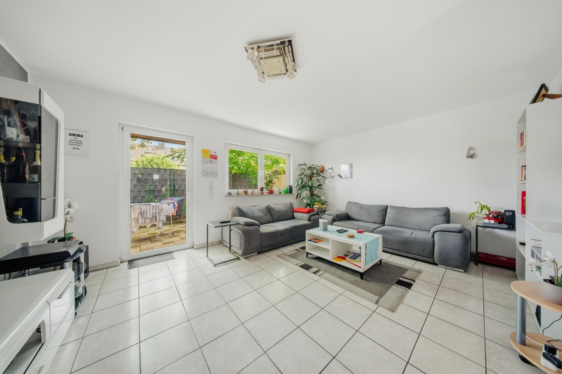 Wohnzimmer mit zwei grauen Sofas, Couchtisch, Fliesenboden und Zugang zur Terrasse.
