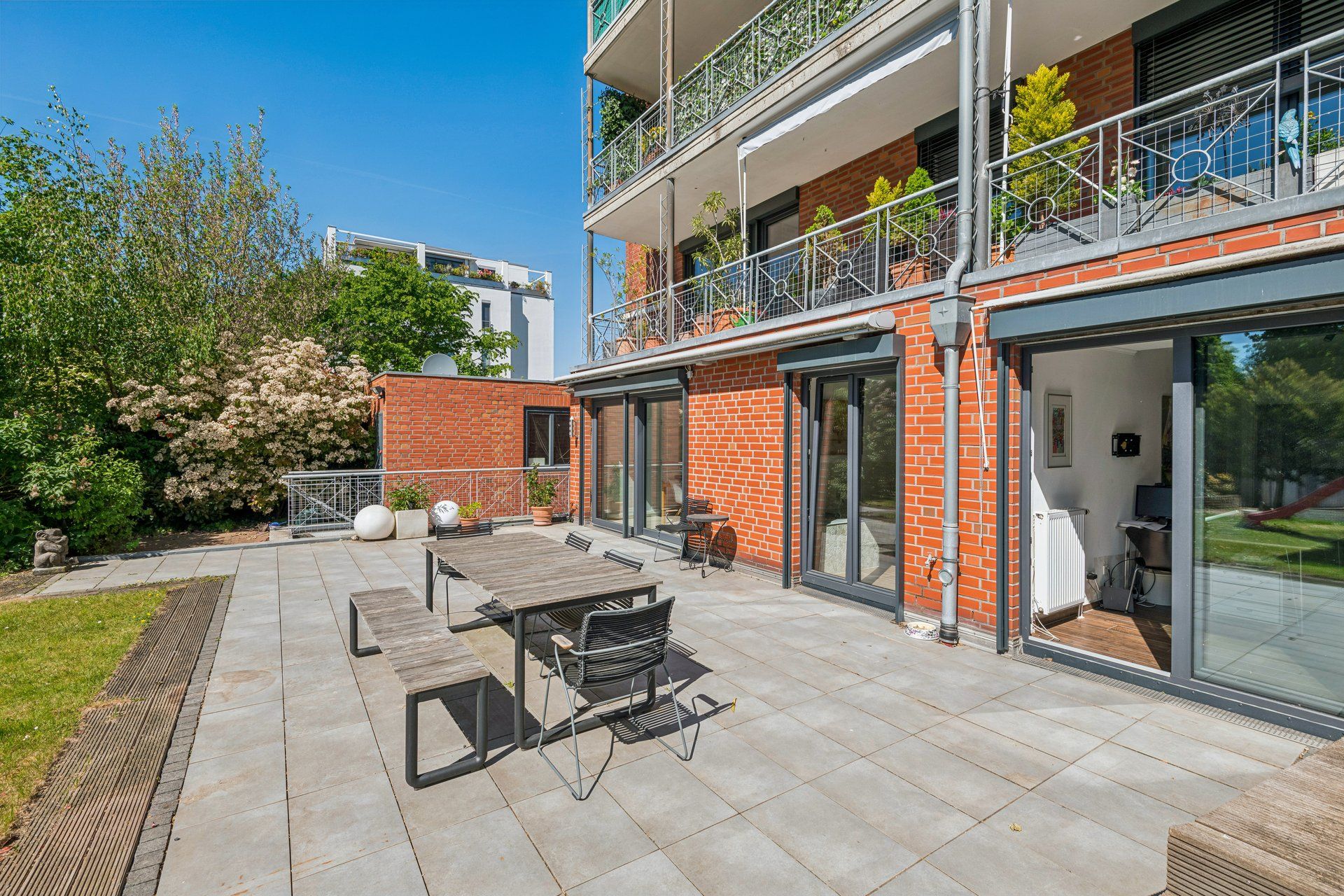 Große Terrasse mit Tisch, Stühlen und Blick auf Garten neben einem modernen Wohngebäude aus Backstein.