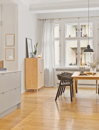 Helle Küche mit Holzboden, Esstisch, schwarzen Stühlen und großen Fenstern.