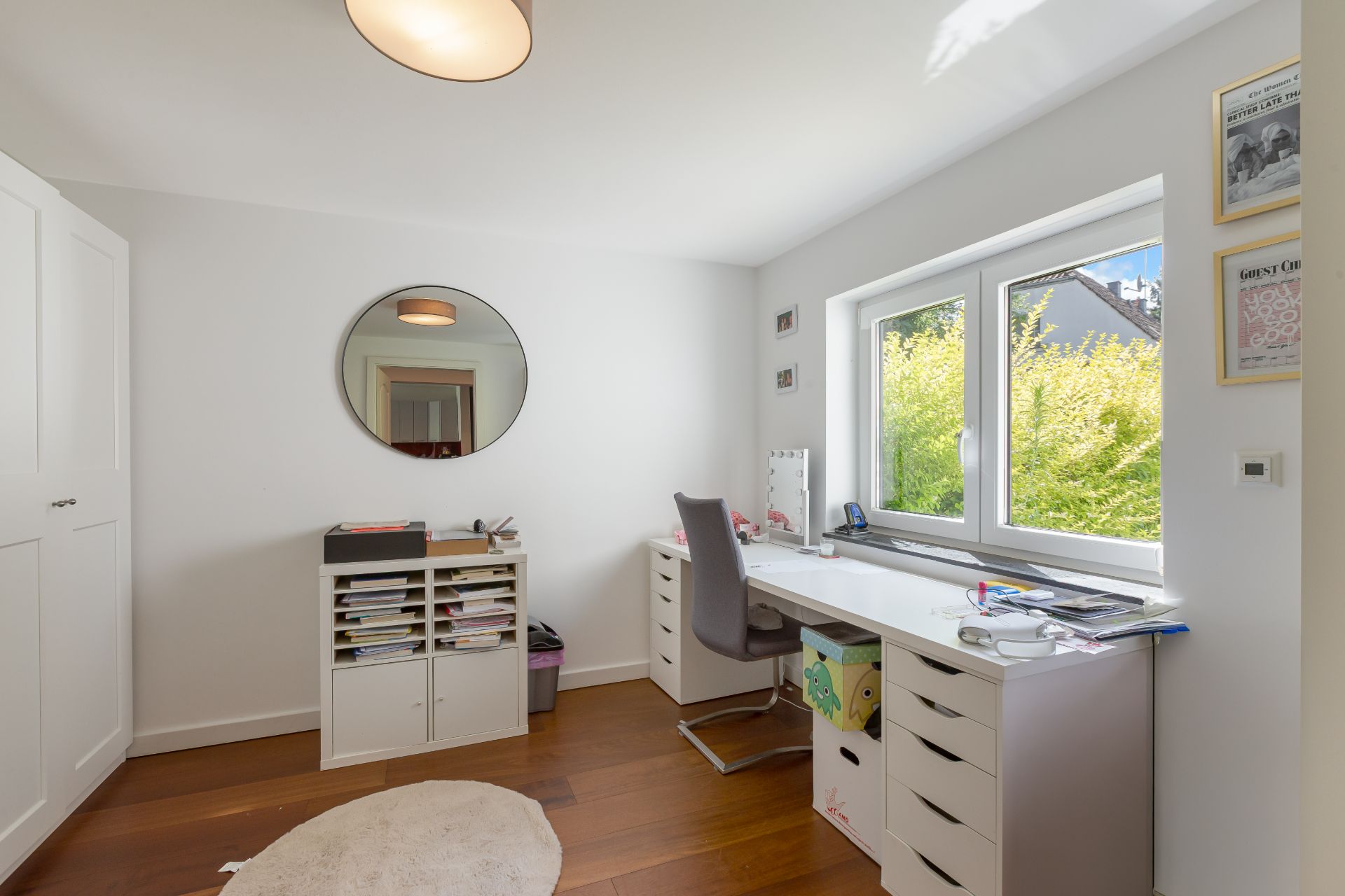 Helles Arbeitszimmer mit Schreibtisch am Fenster, Regal, Spiegel und Holzfußboden.
