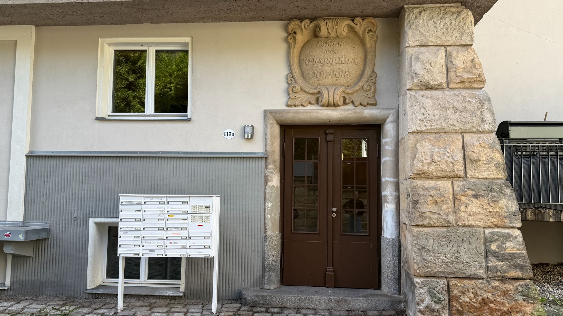 Hauseingang mit brauner Tür, Briefkästen und einem Fenster daneben.
