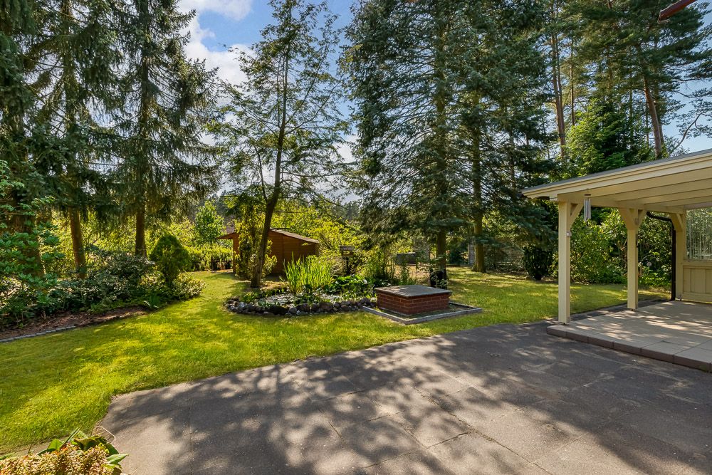 Garten mit Rasenfläche, Bäumen, überdachter Terrasse und kleinem Holzschuppen im Hintergrund.