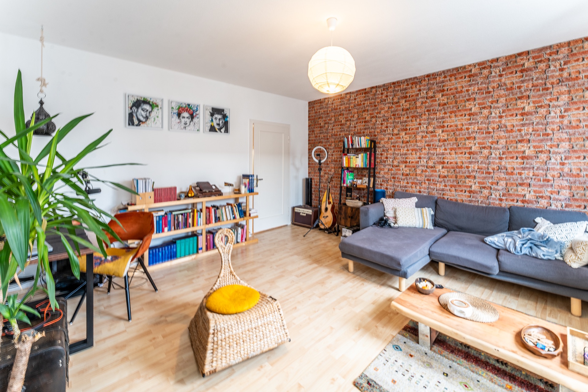 Helles Wohnzimmer mit grauem Sofa, Holztisch, Bücherregalen und Ziegelwand.