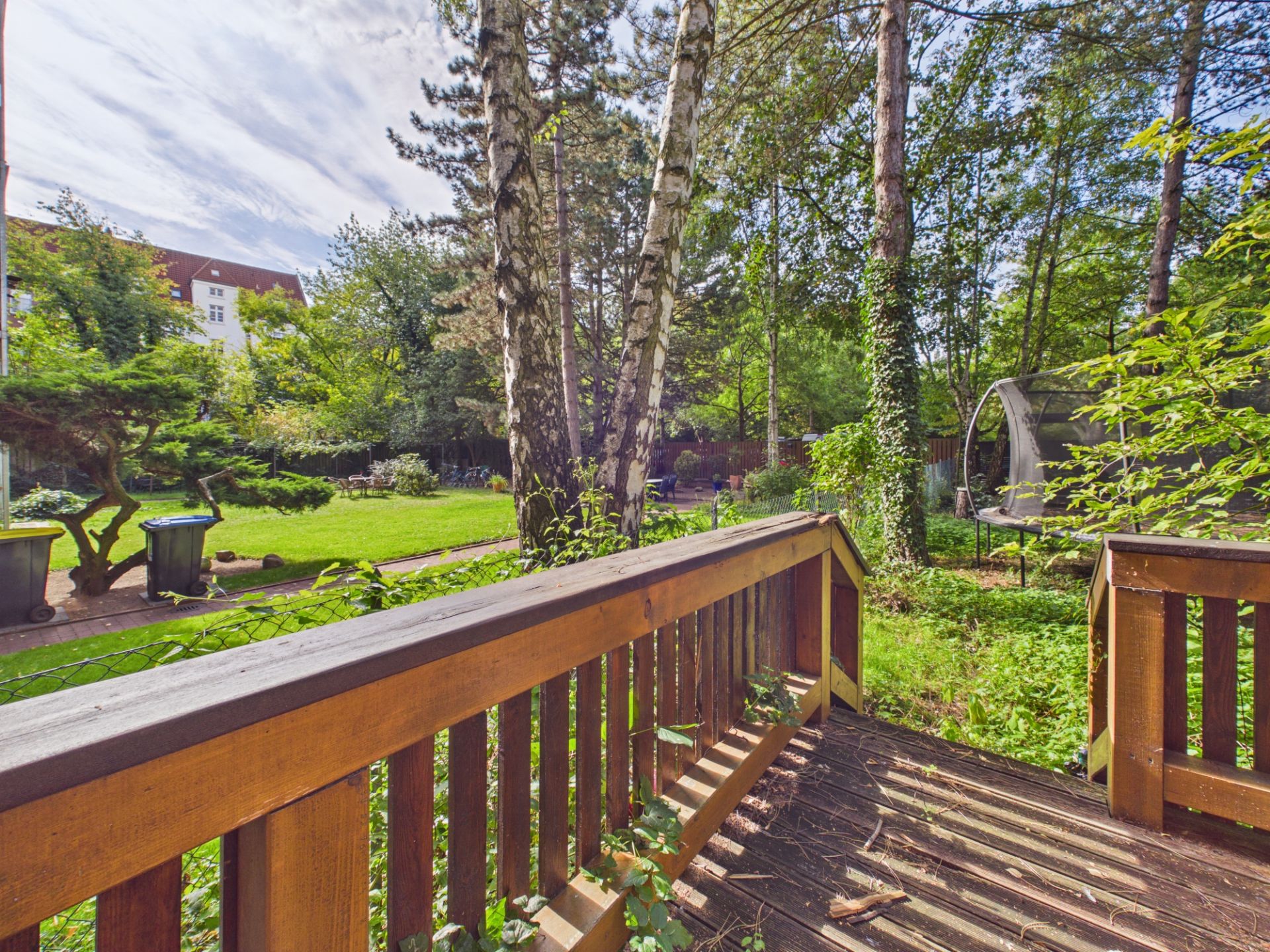 Holzterrasse mit Geländer, Blick auf einen grünen Garten mit Bäumen und Rasen.