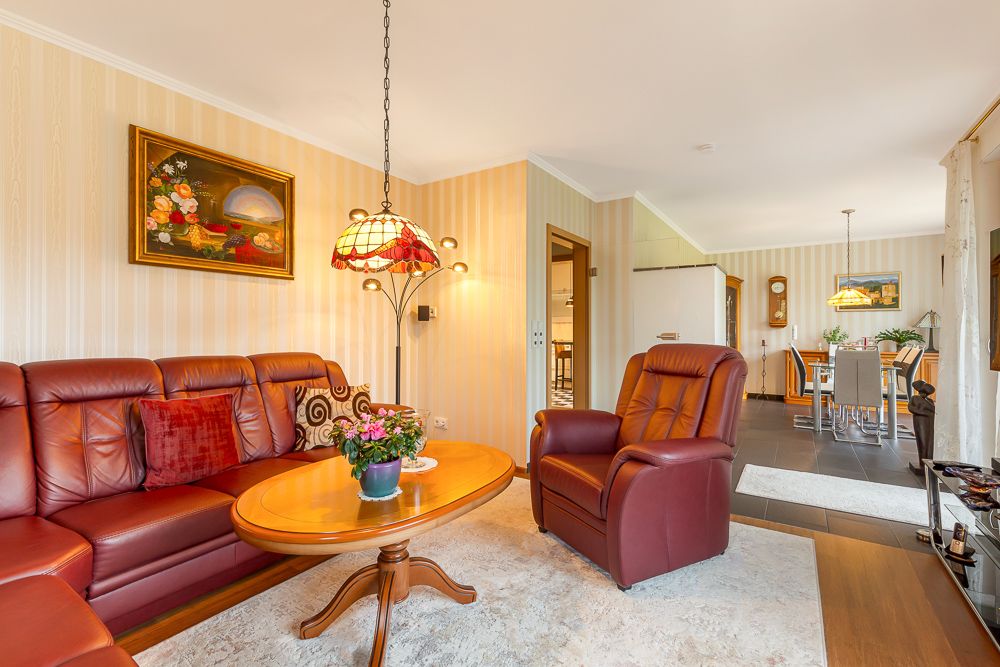 Wohnzimmer mit roten Ledermöbeln, Holztisch, Teppich und Blick in den Essbereich.