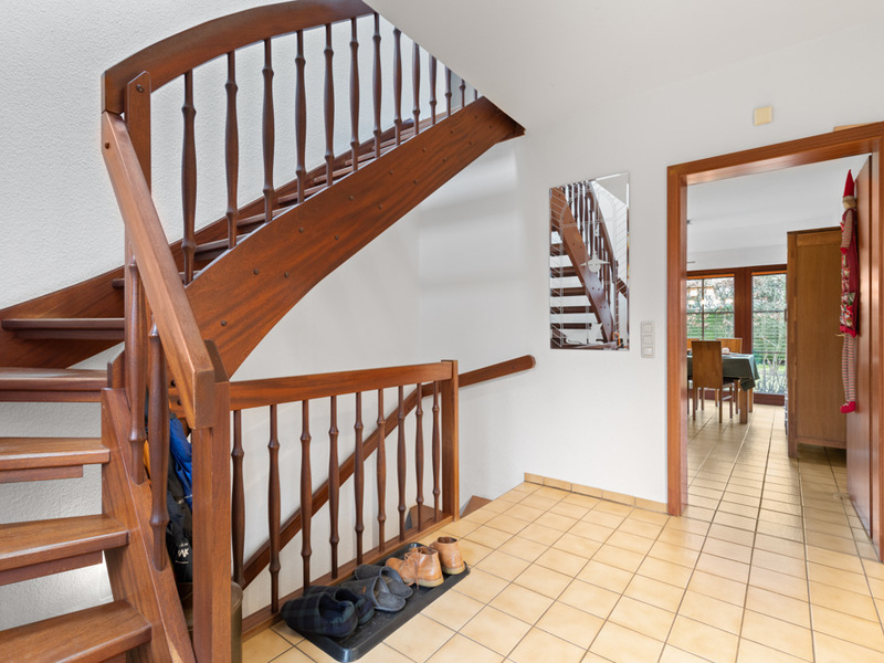 Flur mit Holztreppe, Fliesenboden und einigen Schuhen, Blick in ein Esszimmer.