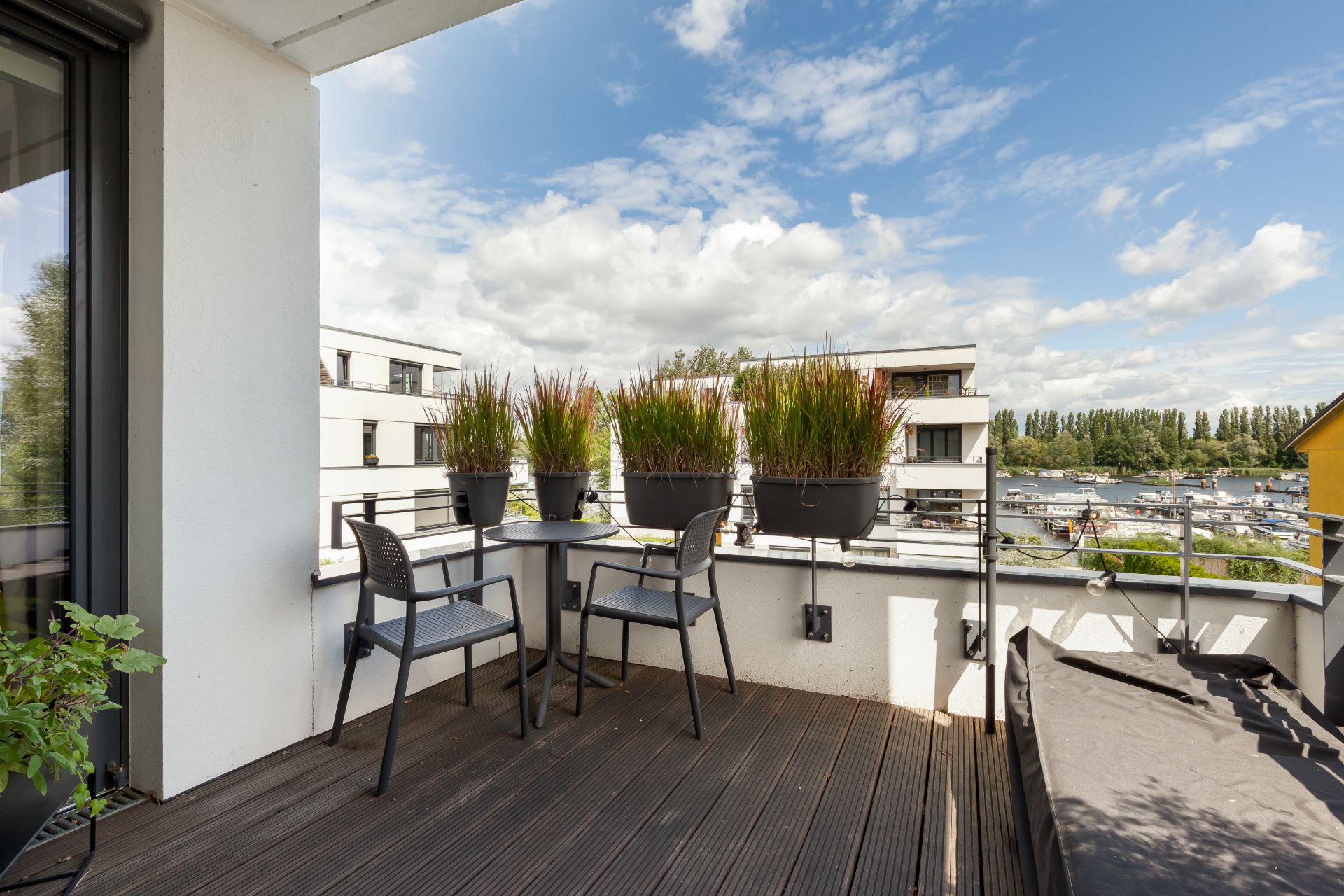 Balkon mit zwei Stühlen, einem Tisch und Pflanzkübeln, Blick auf moderne Wohngebäude.