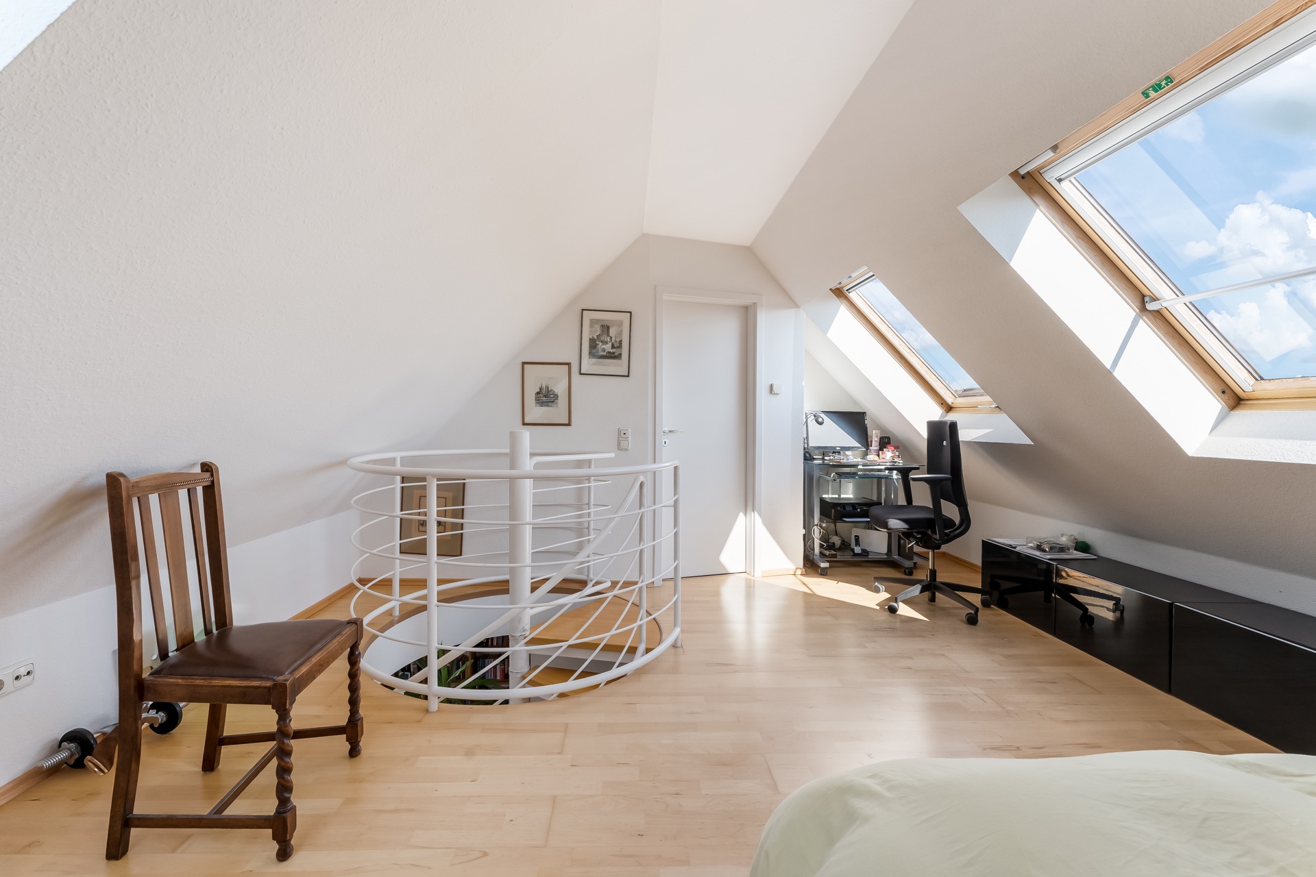 Helles Dachzimmer mit Schreibtisch, Stuhl, Wendeltreppe und großen Dachfenstern.