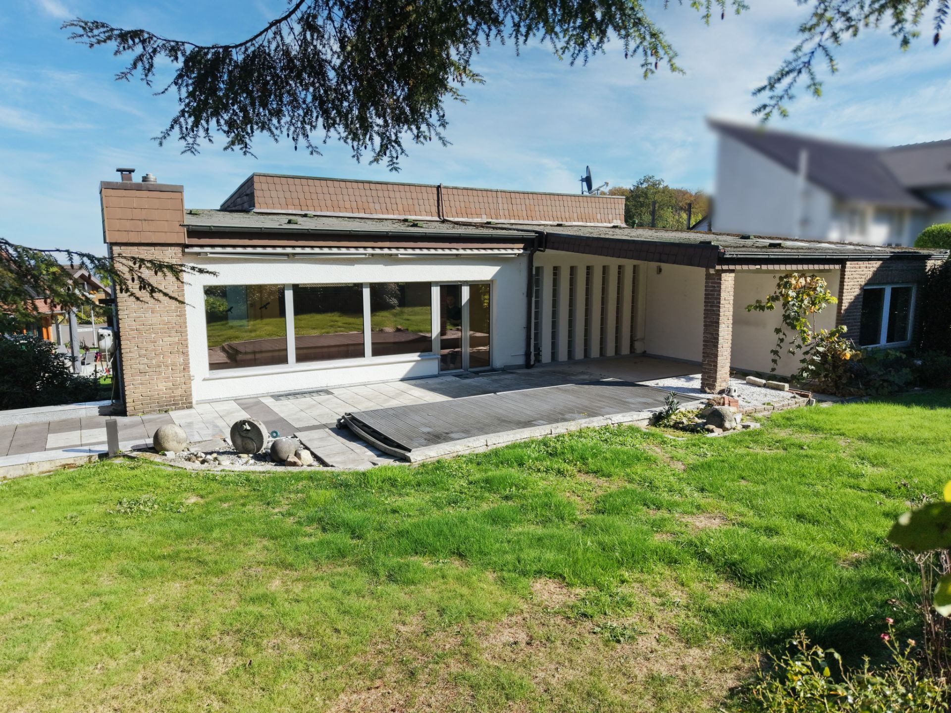 Einfamilienhaus mit großer Fensterfront und überdachter Terrasse, umgeben von Rasen und Garten.