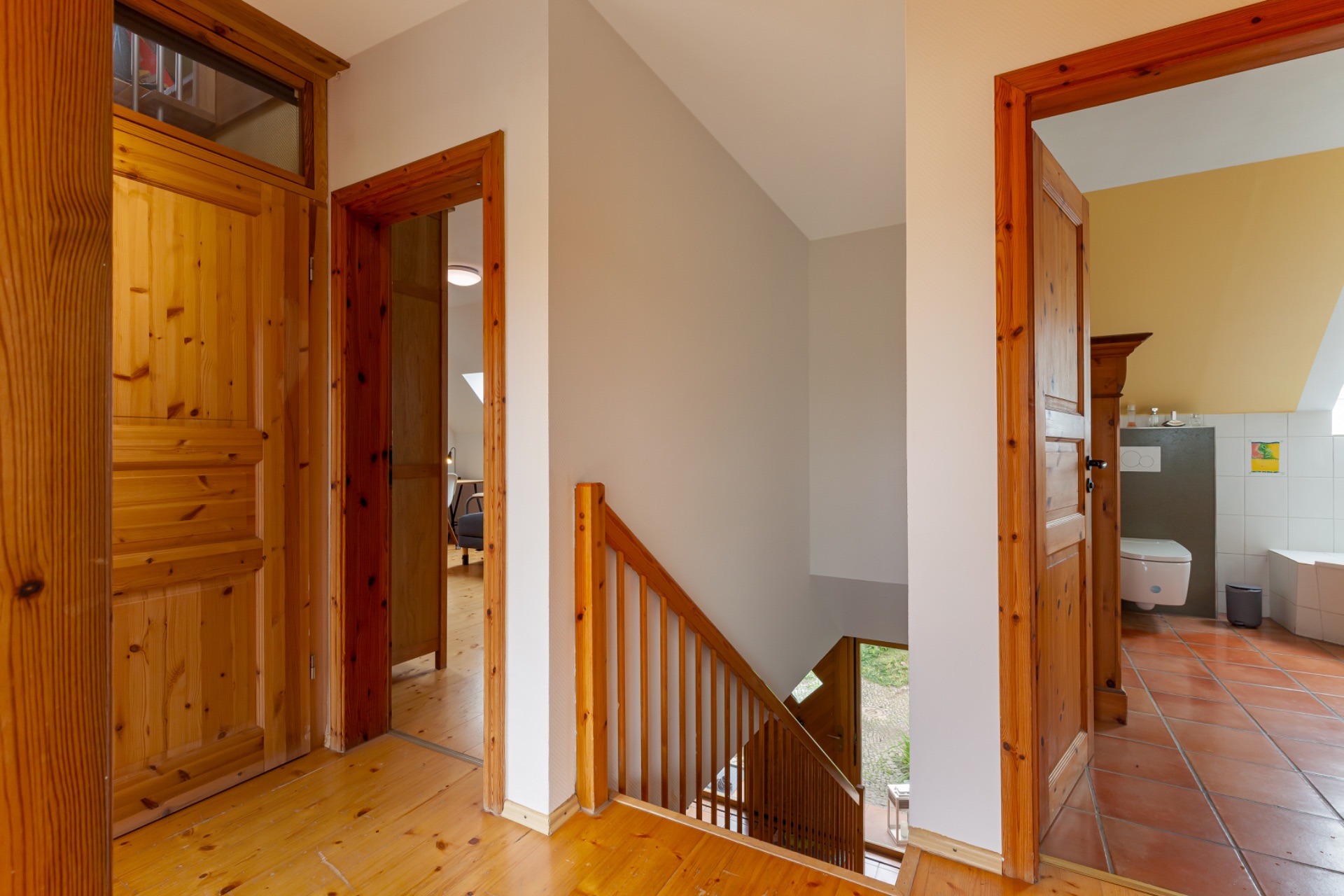 Flur mit Holztüren, Treppe und Blick in ein Badezimmer mit Fliesenboden.