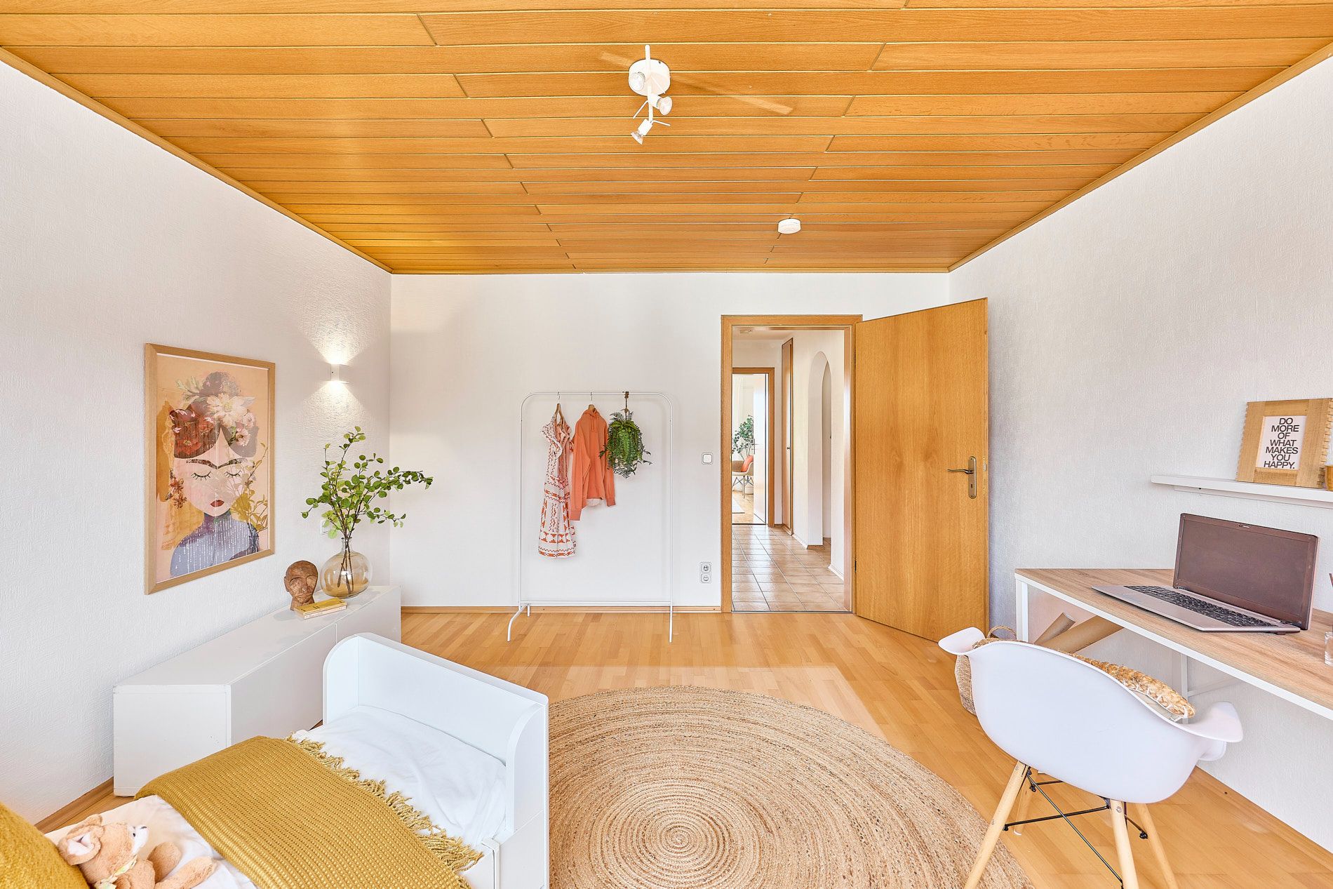 Helles Kinderzimmer mit Holzboden, Schreibtisch, Bett, offenem Kleiderständer und Dekoration.