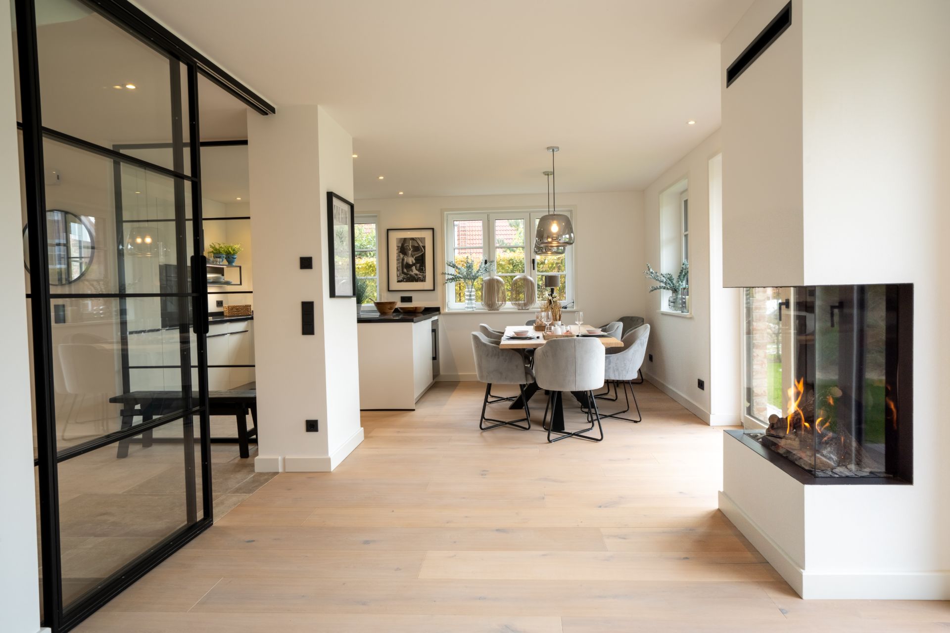 Heller Essbereich mit rundem Tisch, Kamin und großen Fenstern in modernem Wohnraum.