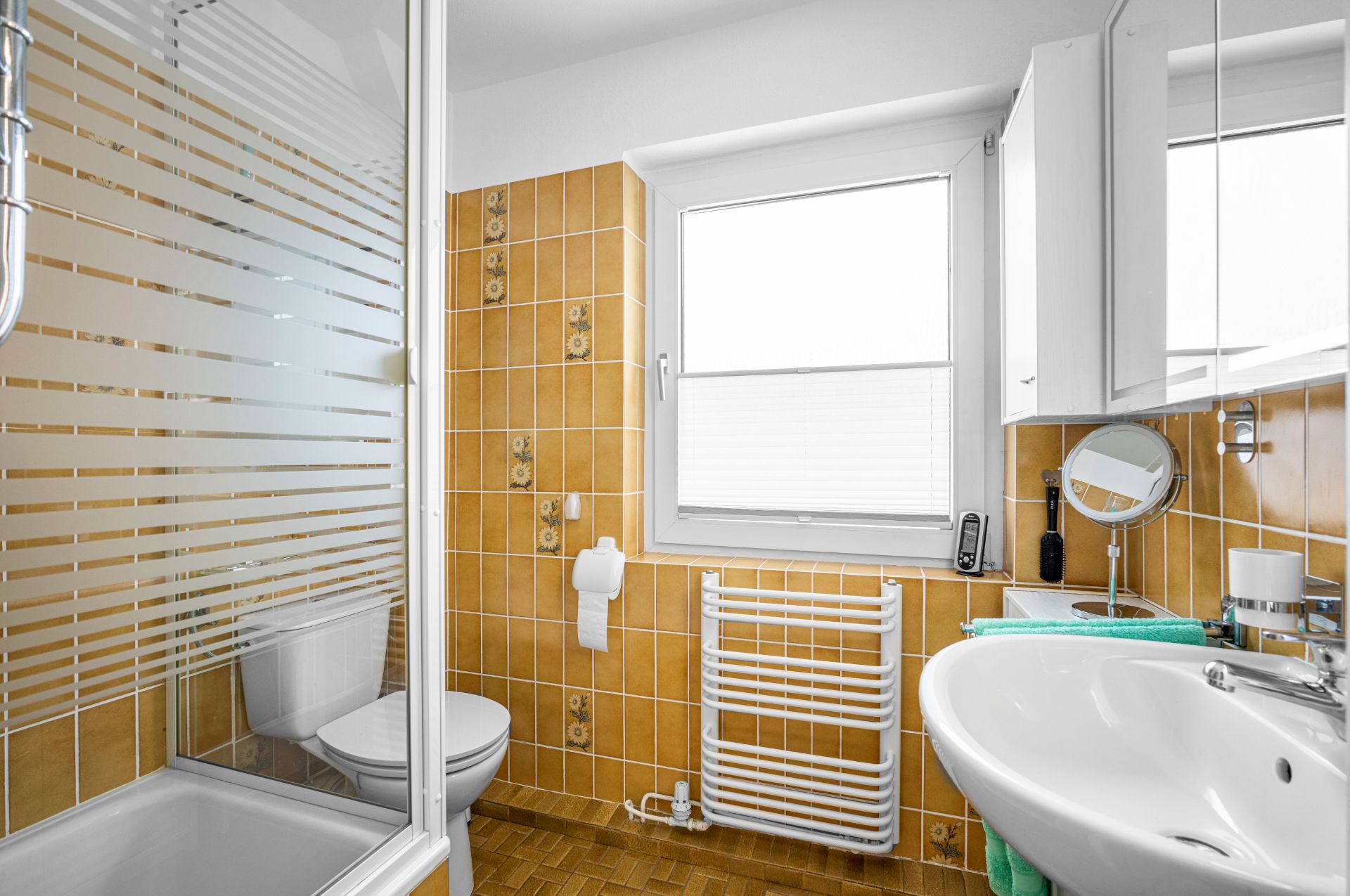 Helles Badezimmer mit orangenen Fliesen, Dusche, WC, Waschbecken und Fenster.