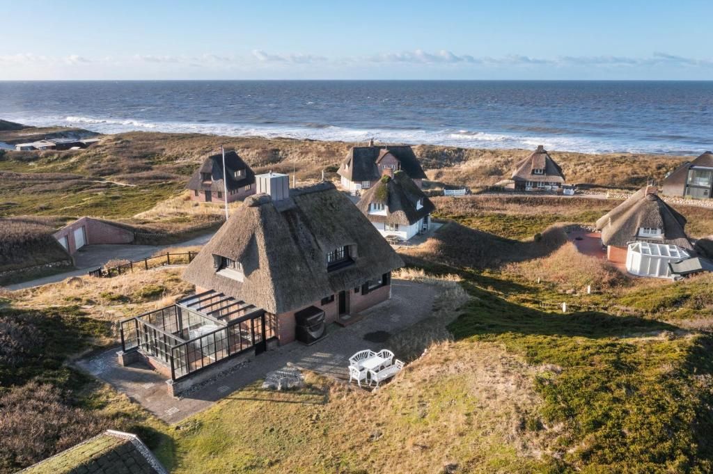 Haus mit Reetdach und Terrasse nahe der Küste, umgeben von weiteren Häusern und Meerblick.