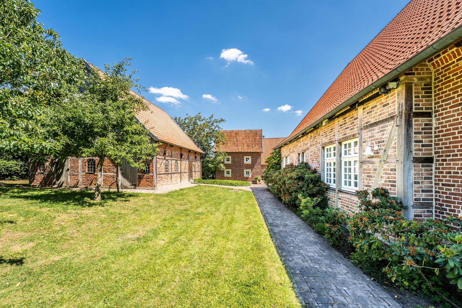 Gepflegter Innenhof mit drei Backsteingebäuden und grünem Rasen unter blauem Himmel.