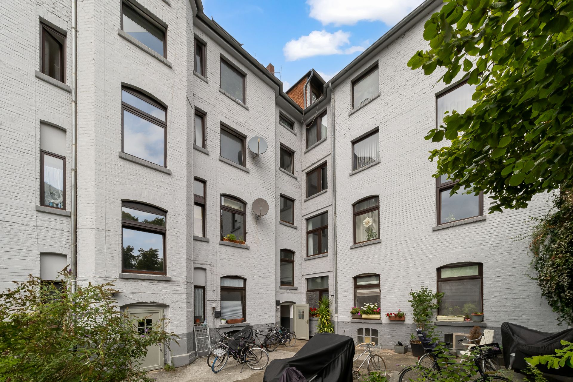 Innenhof eines Wohnhauses mit weißen Wänden, Fenstern und mehreren abgestellten Fahrrädern.