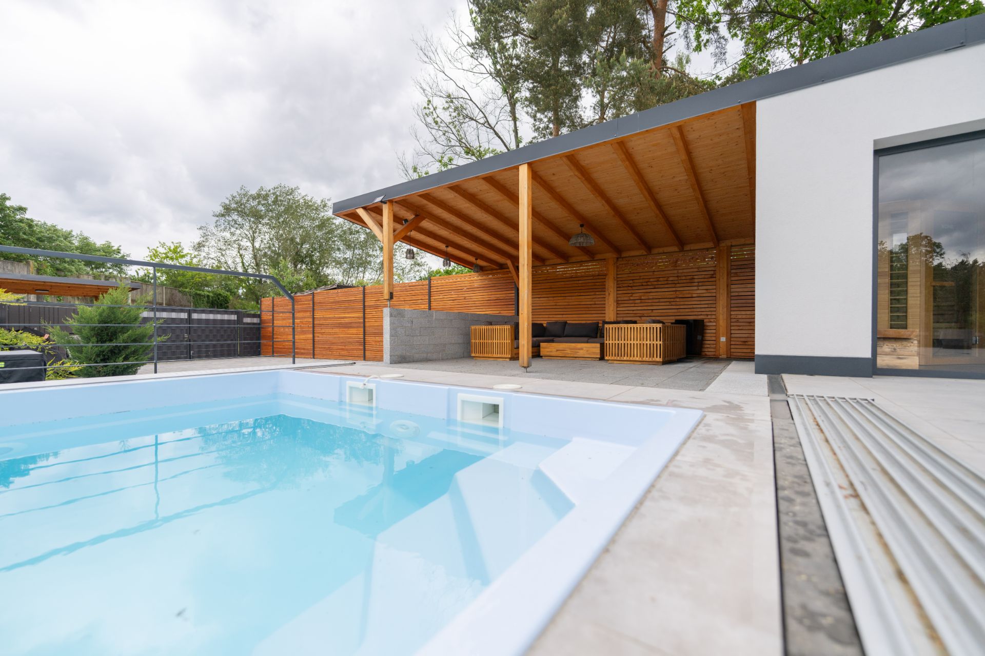 Moderner Garten mit Pool und überdachter Terrasse mit Sitzmöbeln neben einem Haus.
