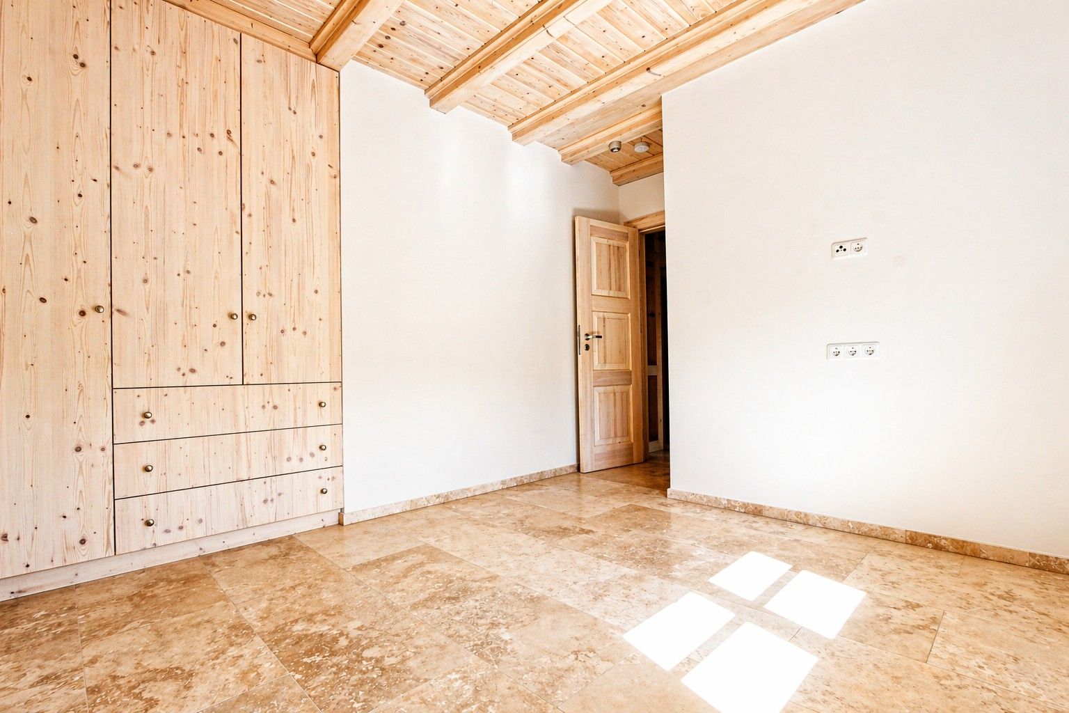 Leeres Zimmer mit Holzboden, Holzdecke und Einbauschrank, offene Tür im Hintergrund.