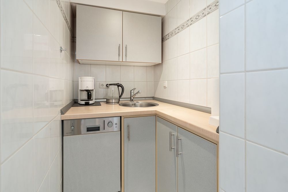 Kleine Küchenecke mit Spüle, Kaffeemaschine, Wasserkocher und Oberschränken.
